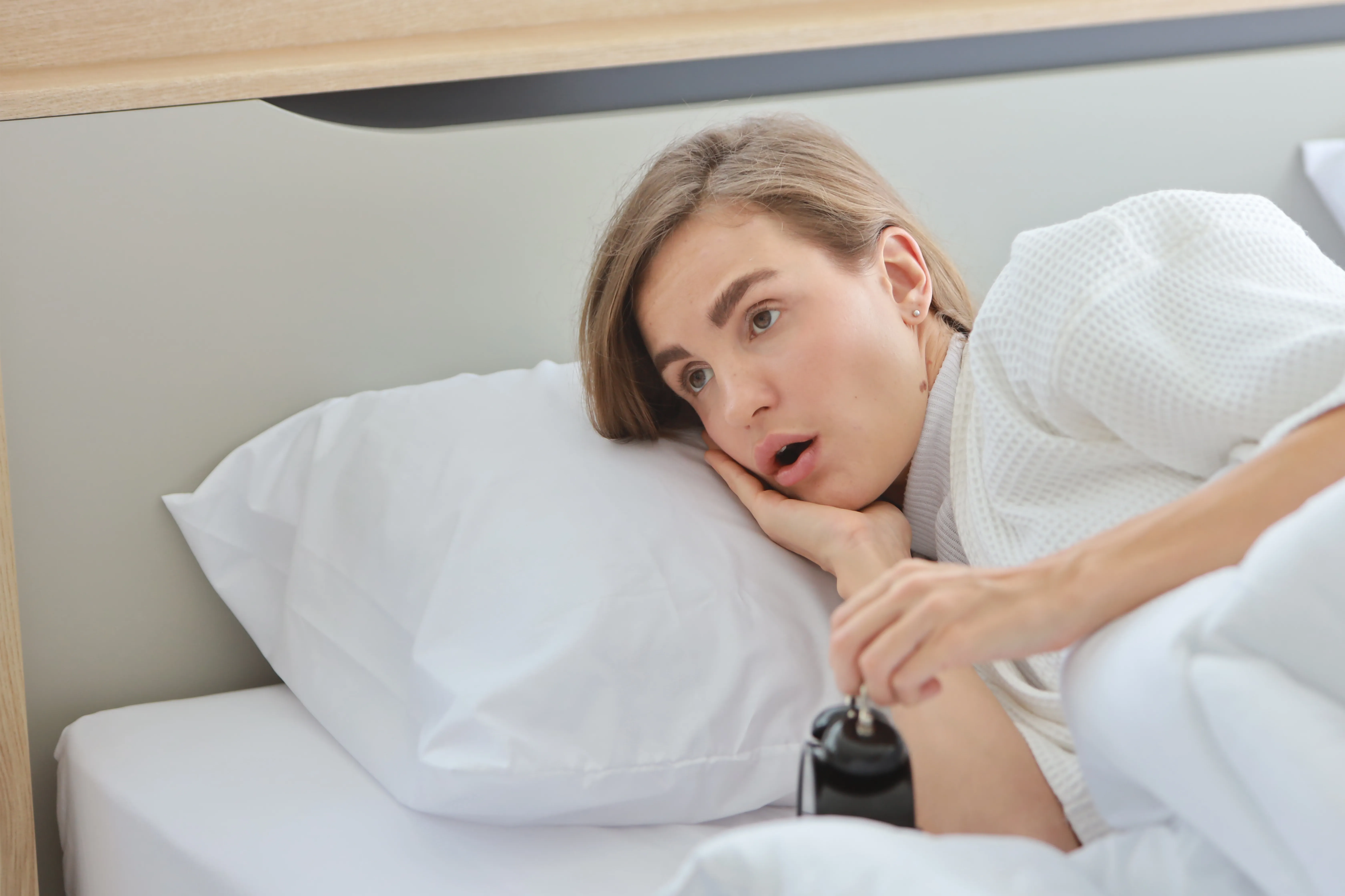 Upset Young Caucasian Woman In White Sleepwear Lying In Bed